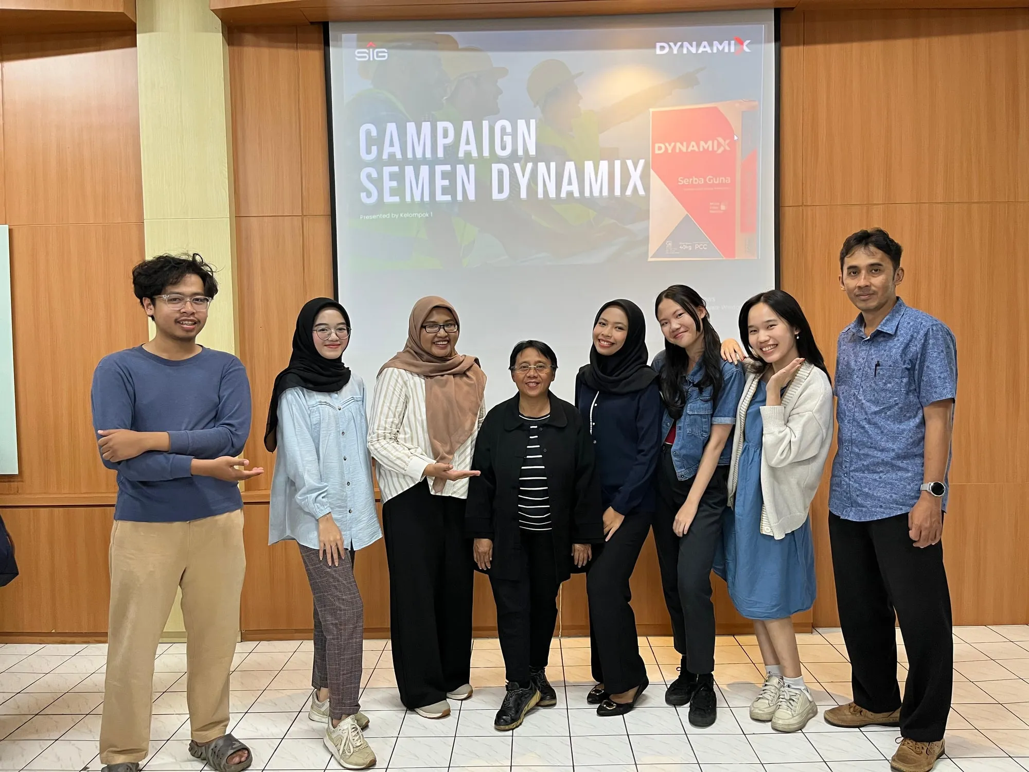 Nine people stand smiling in a row in front of a projected slide that reads 'Campaign Semen Dynamix', after the presentation.